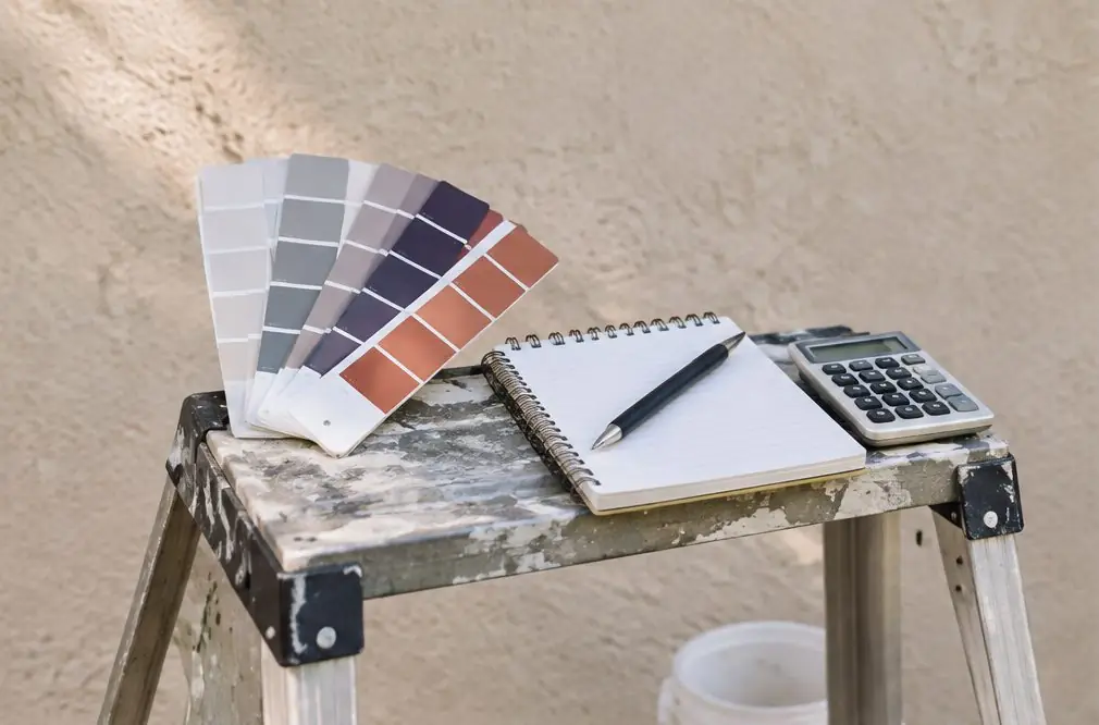 Illustration: a paint chart, a notepad and a calculator on a stepladder in front of a plain stucco wall